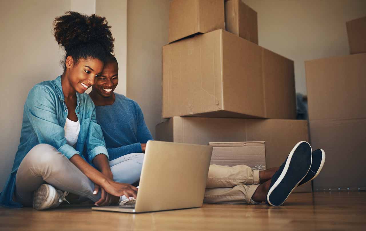 Couple staring at laptop on the floor with cardboard boxes next to them.